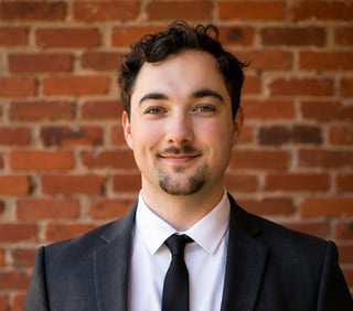 Professional portrait of a man in business suit and tie smiling at camera against brick wall background