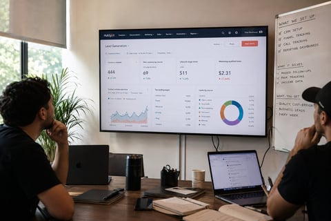 Two people reviewing analytics dashboard on wall-mounted monitor in office